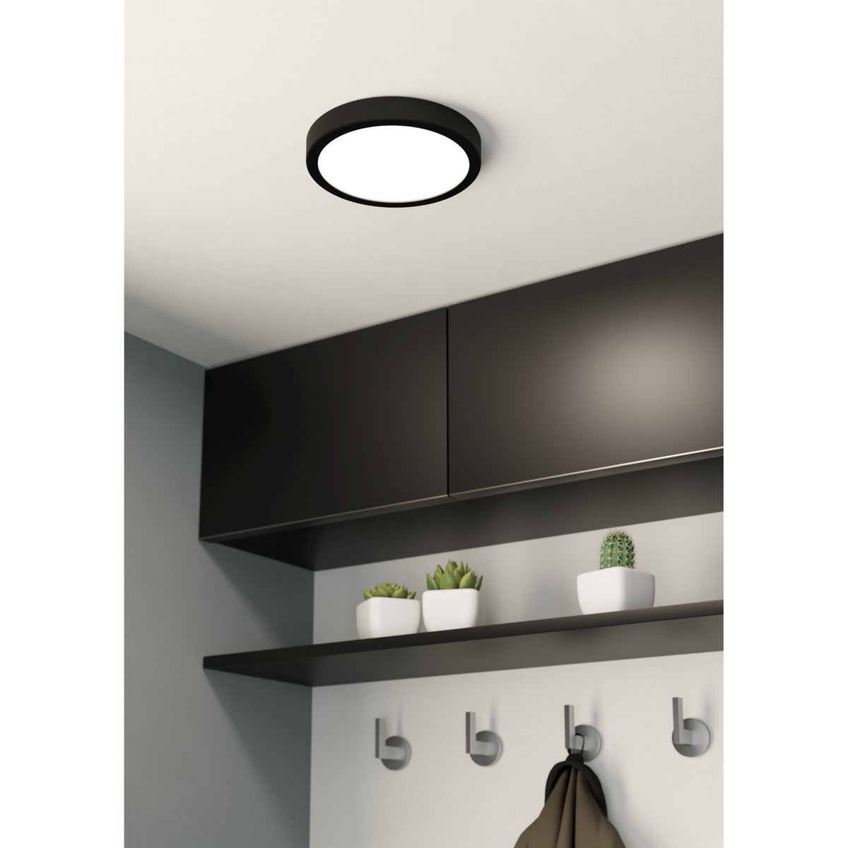 Gosmelle round LED downlight with black steel surround and white opal diffuser, fitted on a ceiling above dark wall cabinets in a kitchen or hallway setting.