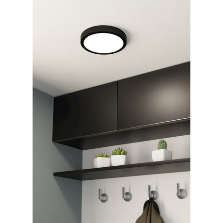 Gosmelle round LED downlight with black steel surround and white opal diffuser, fitted on a ceiling above dark wall cabinets in a kitchen or hallway setting.