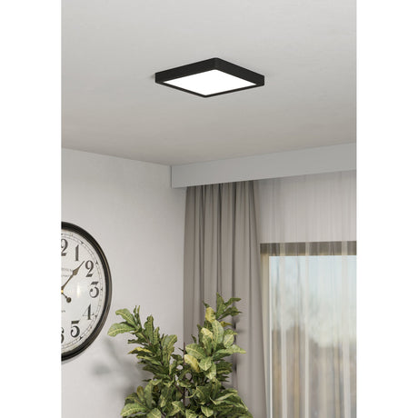 Gosmelle square LED downlight in black with white diffuser, surface-mounted on a ceiling above a curtained window in a living room setting.