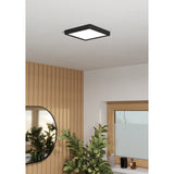 Gosmelle LED Downlight, 22 x 22cm square fixture with matt black frame and white diffuser, mounted on a white ceiling in a bathroom with wood-panelled wall and plants below.