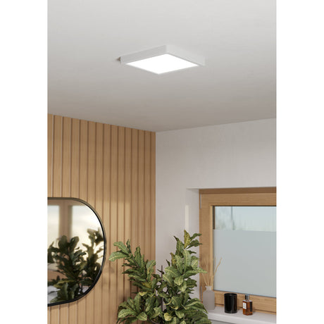 Gosmelle LED Downlight, a square white 22 x 22cm ceiling-mounted panel shown flush-fitted in a bathroom ceiling above wood-panelled walls and a window.