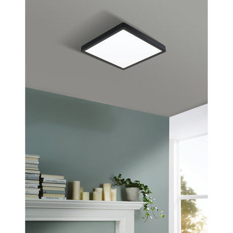Gosmelle square LED downlight with slim black steel body and white plastic diffuser, mounted flush on a grey ceiling above a green-walled room with mantel decor.