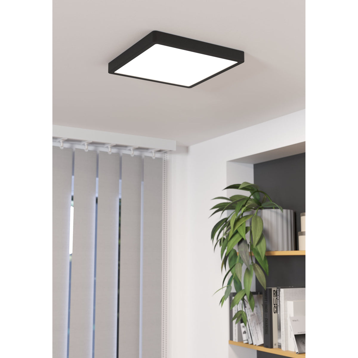 Gosmelle square LED downlight with black steel frame and white plastic diffuser, mounted on a living room ceiling above a bookshelf with plants.