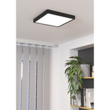 Gosmelle square LED downlight with black steel frame and white plastic diffuser, mounted on a living room ceiling above a bookshelf with plants.