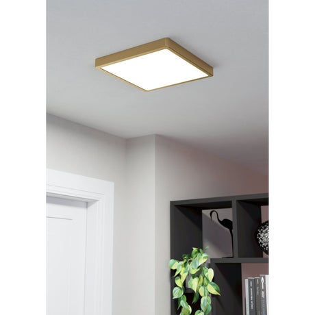 Gosmelle LED Downlight in brushed brass, a square surface-mounted ceiling fixture with white diffuser, shown lit in a modern hallway near a dark bookshelf.