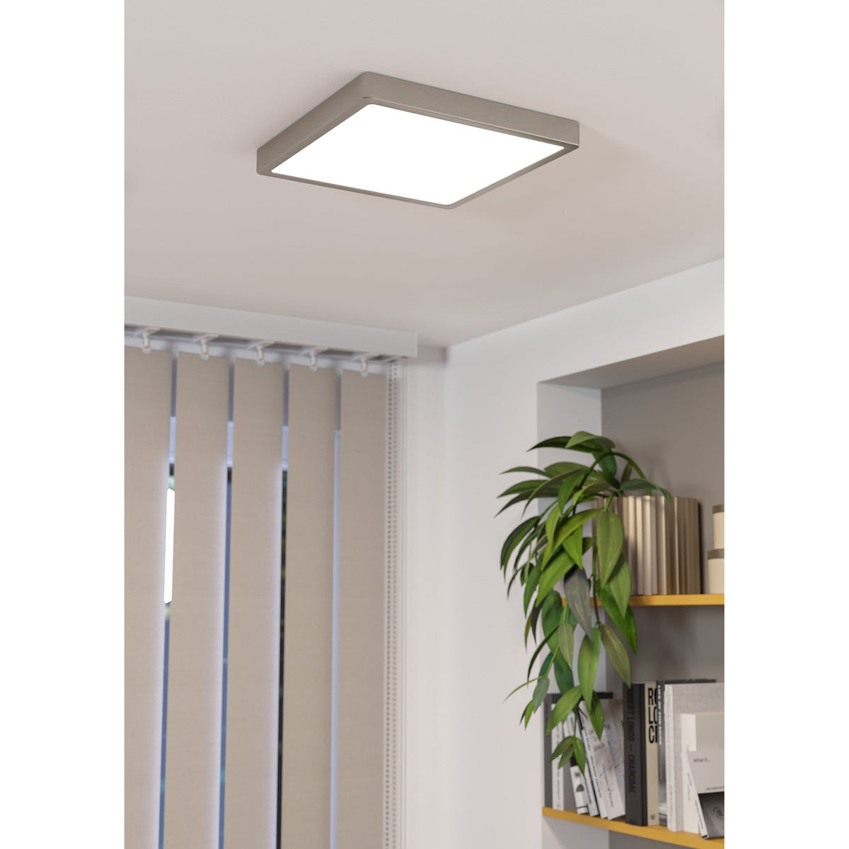 Square LED downlight with slim satin nickel frame and flat white diffuser, mounted on a living room ceiling near shelving and vertical blinds.