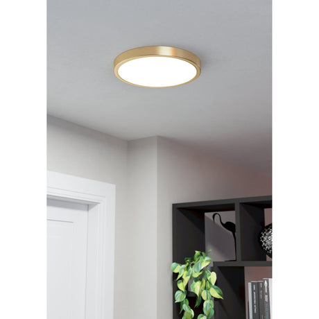 Gosmelle LED downlight in brushed brass, 28.5cm round flush fitting with white diffuser, shown on a grey ceiling above a hallway and shelving unit.