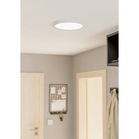 Gosmelle 28.5cm round LED downlight in white, fitted flush to a hallway ceiling with a white steel body and plastic diffuser, shown above doors and a pinboard.