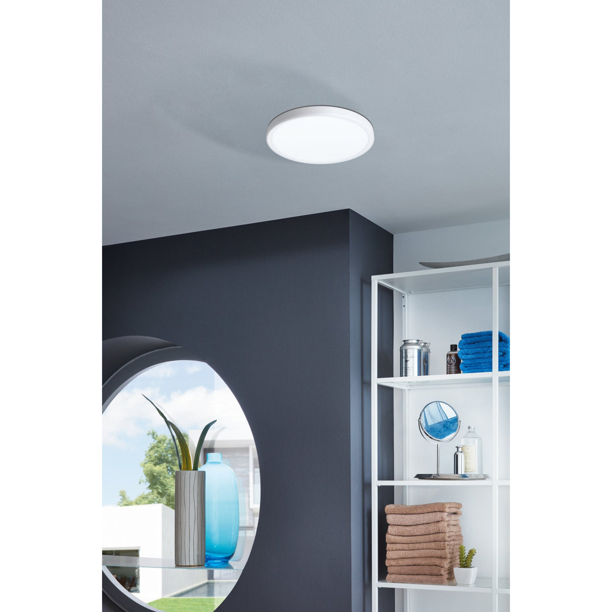 Gosmelle LED downlight, round white surface-mounted fixture on a bathroom ceiling, shown near a dark feature wall, round mirror, and white shelving unit.