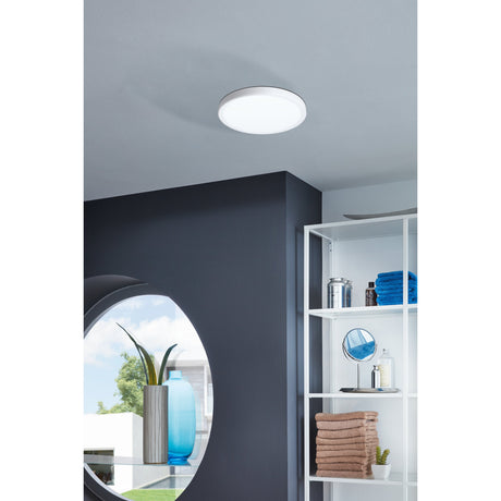 Gosmelle LED downlight, round white surface-mounted fixture on a bathroom ceiling, shown near a dark feature wall, round mirror, and white shelving unit.