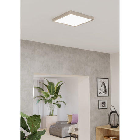Gosmelle square LED downlight in satin nickel steel with white diffuser, flush-mounted on a living room ceiling above a hallway with plants and framed art.