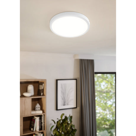 Gosmelle 40cm LED downlight with white aluminium rim and plastic diffuser, flush-mounted on a living room ceiling near a bookshelf and curtained window.