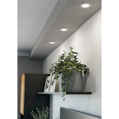 Gosmelle LED downlight in white, 8.8cm round recessed fitting with slim trim, shown installed in a sloped ceiling above a shelf with a plant and framed pictures.