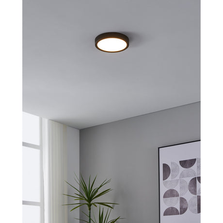 Gosmelle 21cm LED flush ceiling light in black steel with a round white diffuser, shown illuminated on a grey ceiling in a hallway setting.