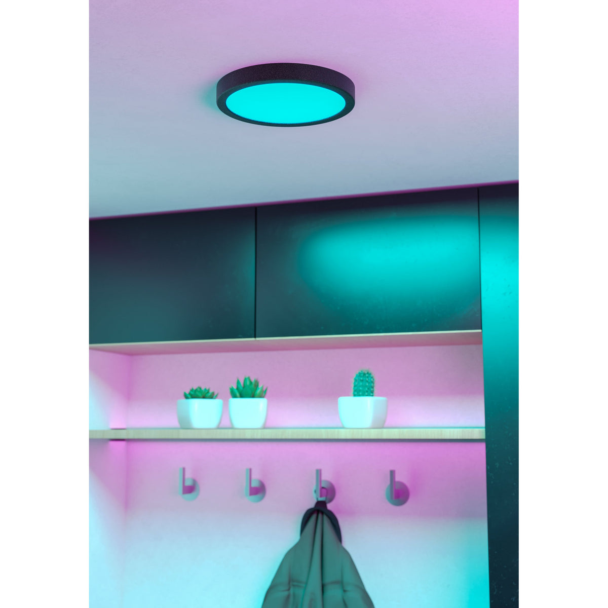 Gosmelle Smart Colour Changing LED Downlight 21.1cm in black, shown recessed in a ceiling glowing turquoise, lighting a hallway with shelf, plant pots and coat hooks below.