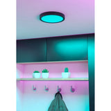 Gosmelle Smart Colour Changing LED Downlight 21.1cm in black, shown recessed in a ceiling glowing turquoise, lighting a hallway with shelf, plant pots and coat hooks below.