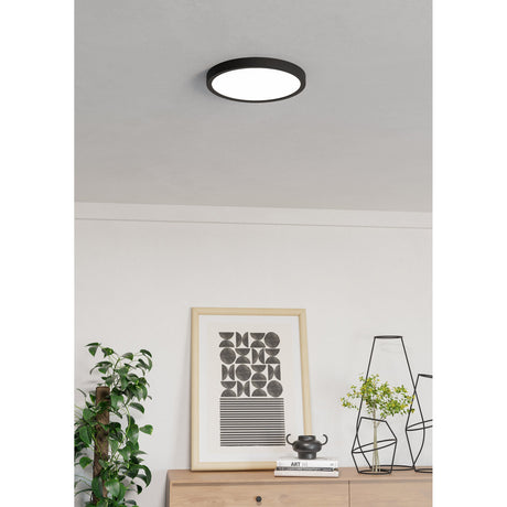 Gosmelle Smart Colour Changing LED Downlight 27.8cm in Black, round flush ceiling fixture with white diffuser, shown installed in a living room above a sideboard with decor.