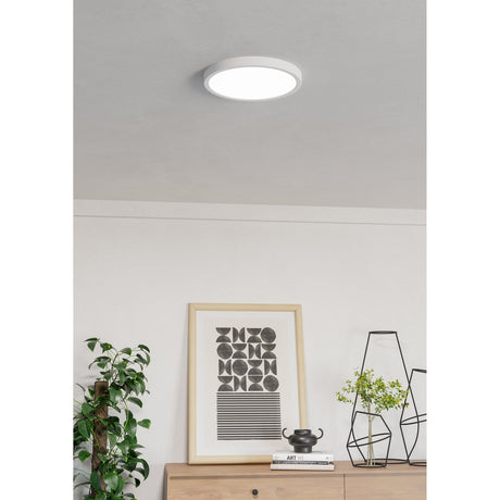 Gosmelle round smart LED downlight in white, 27.8cm, flush-fitted on a light grey living room ceiling above a framed print, plants, and sideboard décor.