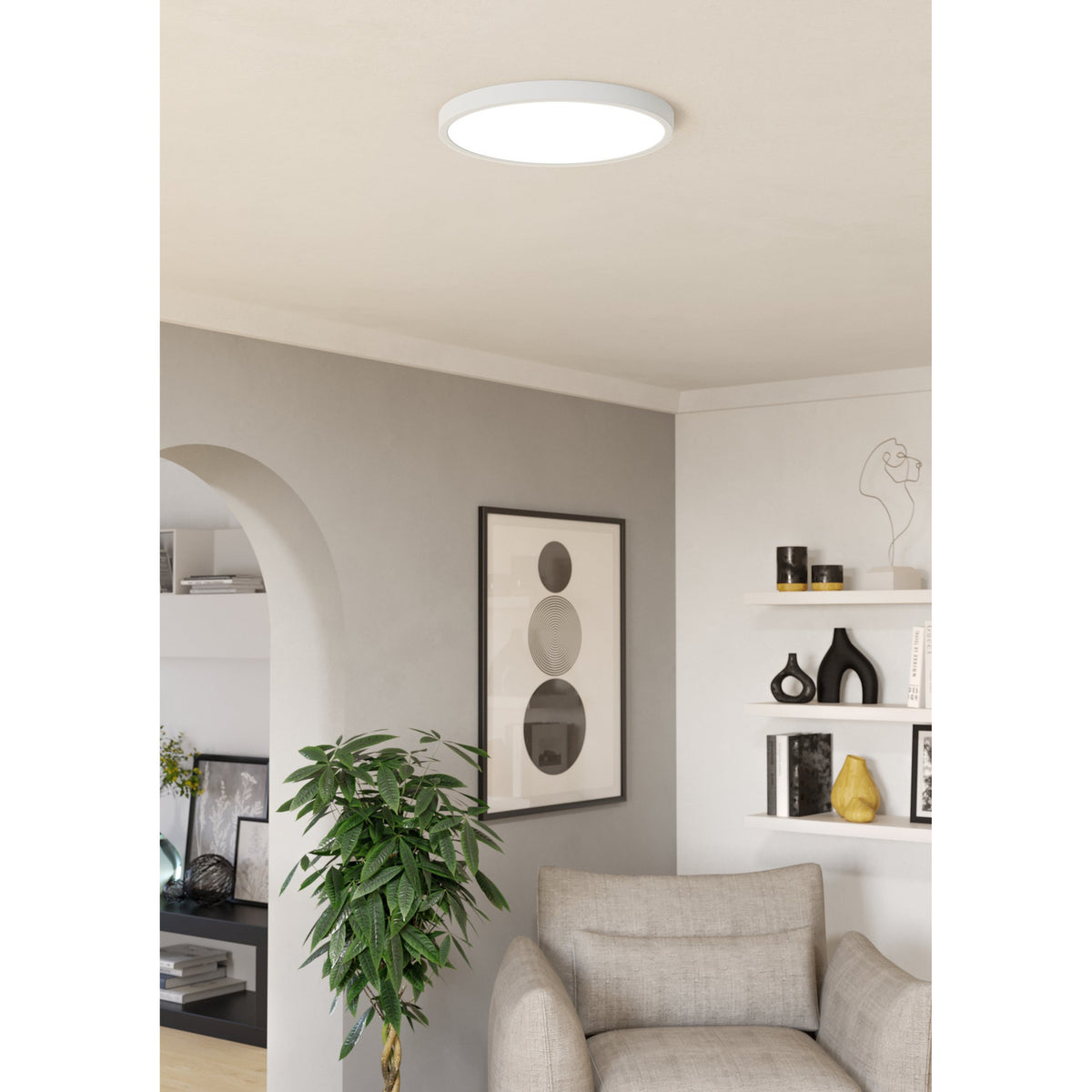 Gosmelle round LED downlight in white, 38.9cm, flush-mounted on a living room ceiling above a seating area with shelving and artwork.