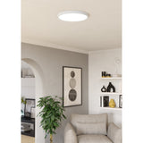 Gosmelle round LED downlight in white, 38.9cm, flush-mounted on a living room ceiling above a seating area with shelving and artwork.