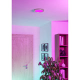 Gosmelle Smart LED Downlight 21.1cm in satin nickel finish, round ceiling-mounted fixture glowing pink, shown in a hallway with doorway, framed art, and shelving.