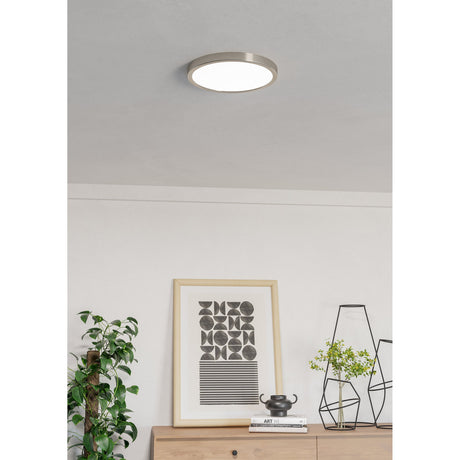 Gosmelle round LED downlight with satin nickel ring and white diffuser, flush-mounted on a living room ceiling above a styled console with artwork and plants.