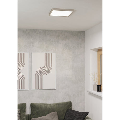 Gosmelle Smart LED Downlight, a slim square satin nickel ceiling fixture with white diffuser, shown fitted above a living room with patterned wall art and a green sofa.