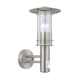 Granette outdoor wall light in stainless steel, with hat-shaped cap, clear glass cylinder shade, exposed bulb, motion sensor, and round wall plate on two arms, shown on a white background.