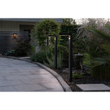 Two Grelbine solar outdoor floor lamps in black aluminium with slim L-shaped posts and rounded tops, lit along a stone garden path at dusk.