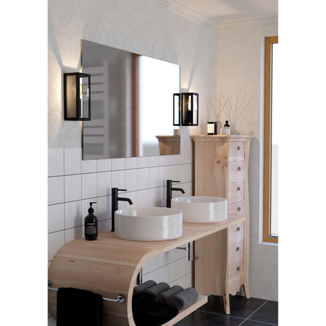 Gromora Bathroom Wall Light in black steel with clear glass panels, shown either side of a mirror above a bathroom vanity with twin countertop basins.