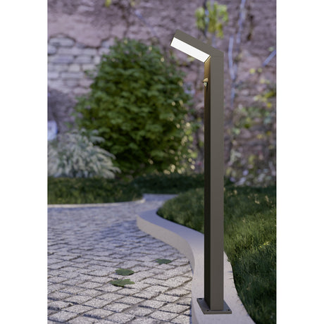 Grottazzolina LED bollard light in black aluminium with angled opal shade and motion sensor, shown beside a garden pathway with lush greenery.