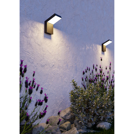 Grottazzolina LED outdoor wall lights in black aluminium with L-shaped profile and opal diffuser, mounted on a textured white wall above lavender and garden shrubs, casting warm downward light.