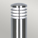 The Sandbanks 1 Light Bollard in silver is a contemporary outdoor lighting fixture featuring a cylindrical design with horizontal rings encircling a frosted light diffuser, and it has an IP44 rating. Its sleek stainless steel finish makes it perfect for placement against a neutral backdrop.