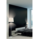 A modern bedroom with a black accent wall, low white bed, dark bedding, and two white lamps—including the Habana Telescopic 1 Light Floor Lamp in White & Chrome—beside a large window letting in natural light.
