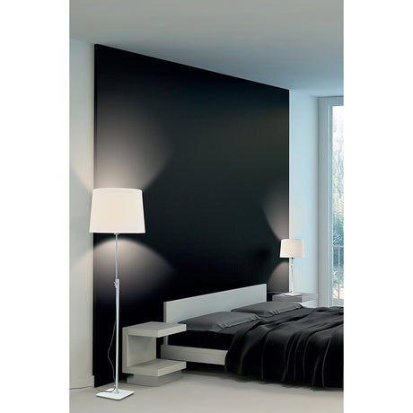 A modern bedroom with a black accent wall, low white bed, dark bedding, and two white lamps—including the Habana Telescopic 1 Light Floor Lamp in White & Chrome—beside a large window letting in natural light.