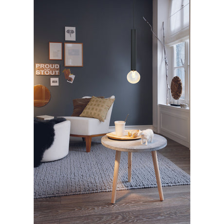 Halmarne Pendant Light in black steel with slim cylindrical shade and exposed E27 bulb, shown above a round wooden coffee table in a living room setting.