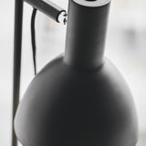 Close-up of the Baltimore Floor Lamp in black, showing the matt black cone shade's rounded shoulder, swivel knuckle, and slim rail against a plain light background.