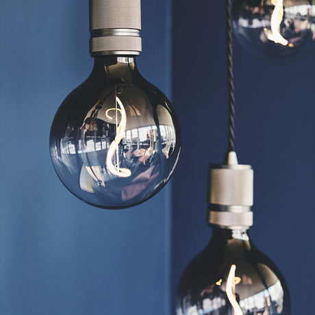 Halo Cable Cord Set E27 pendant lampholders in gunmetal with knurled detailing and twisted black flex, shown lit with globe bulbs against a dark blue wall.