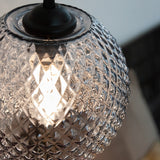 Close-up of the Nobb Ball Pendant Light 22cm in smoke, showing the diamond-cut smoked glass texture, black cap fitting, and lit bulb glowing through the facets.