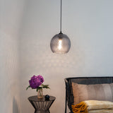 Nobb Ball Pendant Light 22cm in smoke glass with diamond-cut texture and black cap, shown lit above a side table in a living room setting.