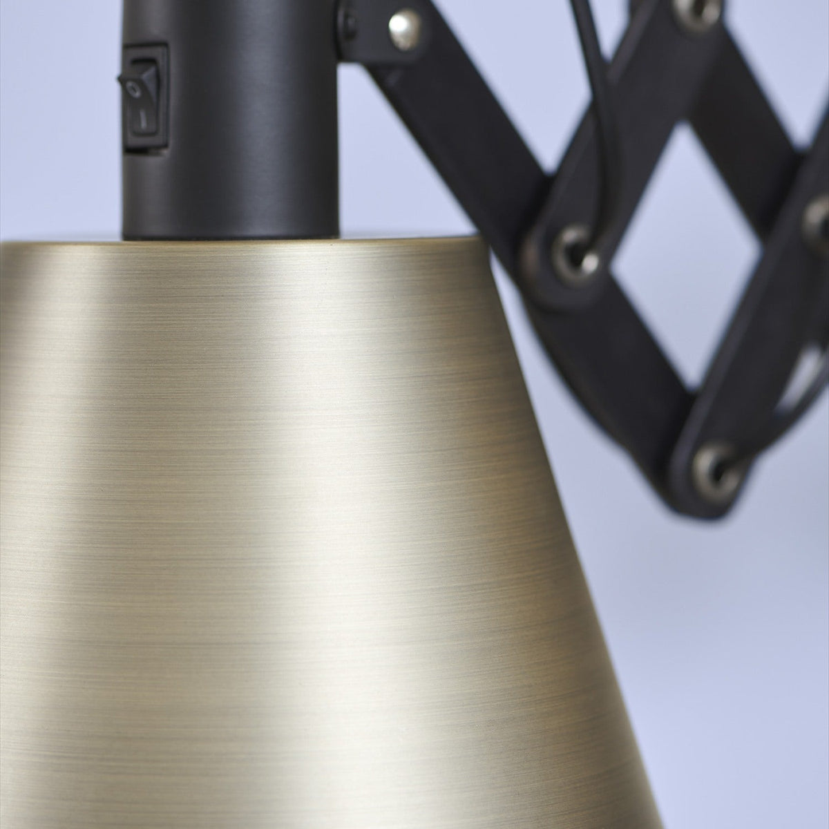 Close-up of the Vintage Oiled Wall Light in black and antique brass, showing the brushed brass cone shade, on/off switch, and scissor arm with riveted lattice joints.