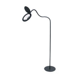 Magni LED X3 Dioptri floor lamp in black, with a round magnifying lens head and hinged cover on a curved slim stem, set on a flat round base against a plain white background.