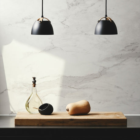 Oslo Pendant Light 16cm in black and oak, two dome shades with arched wood straps hung above a wooden board with a gourd, glass carafe, and black bowl against a marble wall.