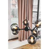 Atom Mini 6 Light Smoke Glass Chandelier in black, with globes branching from a central hub at varied angles, shown lit in a room with pink curtains and a window.