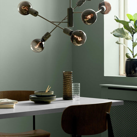 Halo Adjustable 6 Light Chandelier in gunmetal, black rods radiating from a knurled hub with smoked glass globes, shown above a dining table in a sage green room.