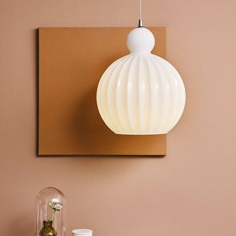 Ball Pendant Light 25cm in Opal, a ribbed white glass globe shade with a small rounded knop, chrome fitting, and twisted flex, shown against a tan wall panel.