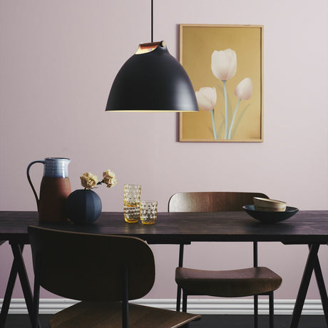 Aarhus Pendant Light 40cm in matt black with a pale oak handle strap and cream-lined dome shade, hung above a dark dining table in a pink-toned room.