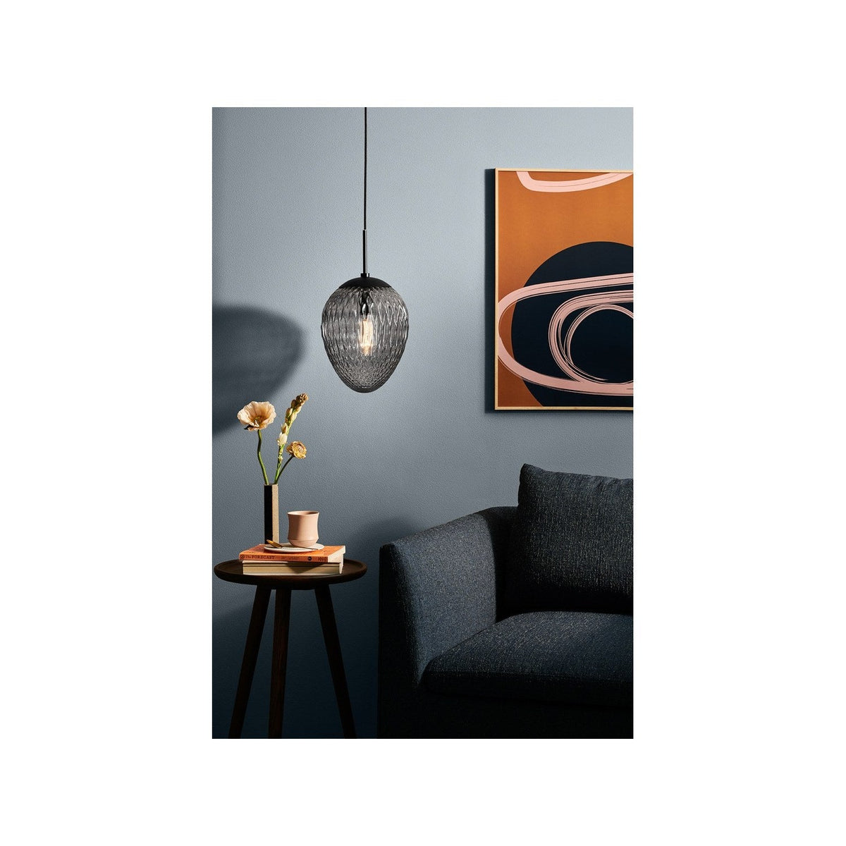 Woods Pendant Light 25cm in smoke glass with a diamond-cut egg-shaped shade, hung above a side table in a grey-walled living room setting.