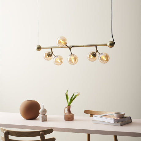 Atom Mini Horizontal 6 Light Chandelier in antique brass with amber glass spheres, hung above a dining table styled with vases and decor.