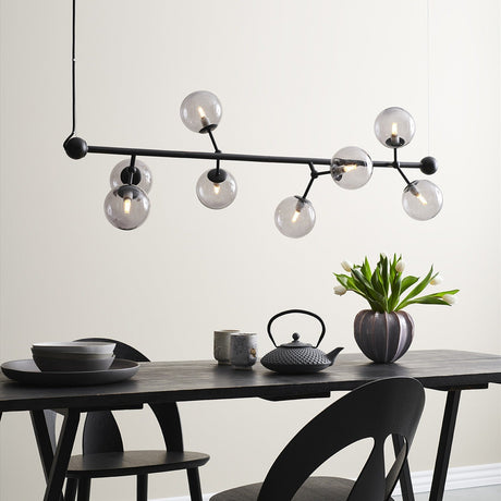 Atom Maxi Horizontal Glass 8 Light Chandelier in black and smoke, a horizontal bar with branching stubs and clear glass spheres, shown suspended over a dining table.